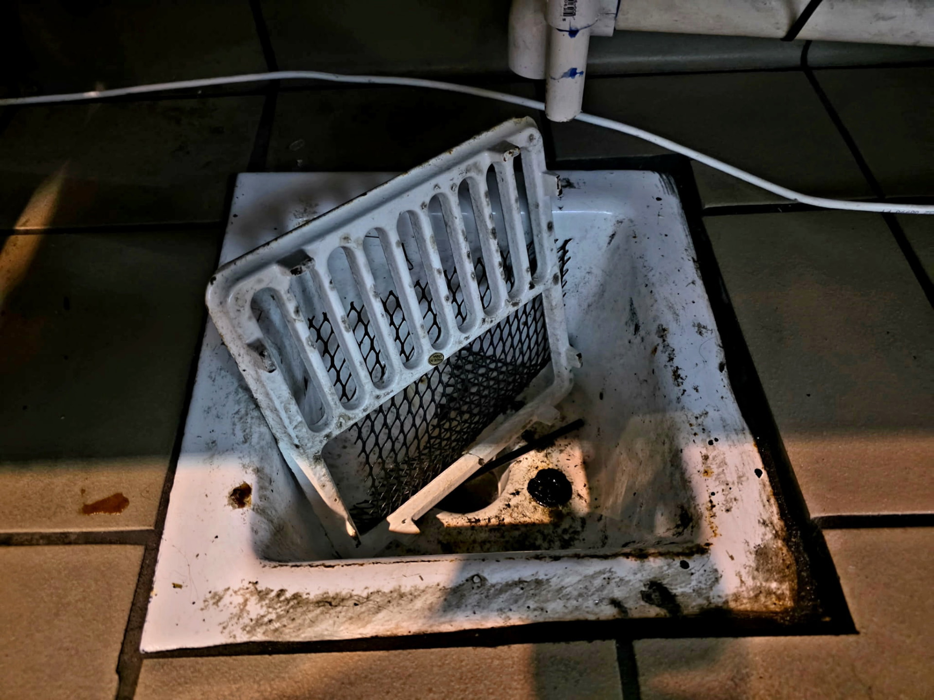 Commercial kitchen floor drain clogged with grease and debris before cleaning